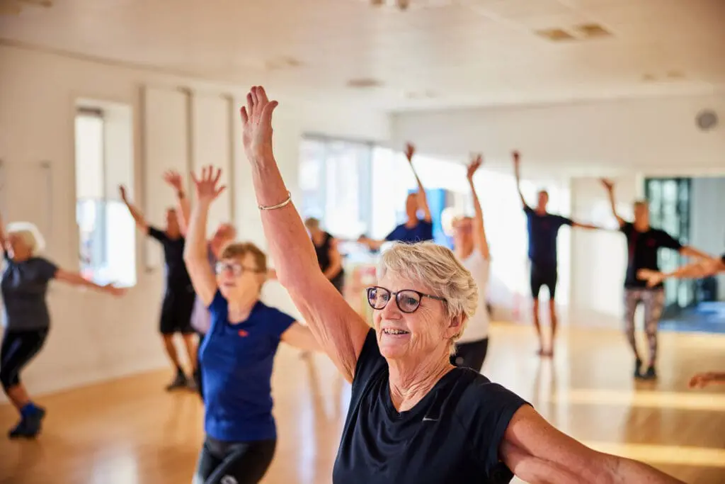 The Best Group Exercise Classes for Seniors That Empower Senior Wellness 2 Smiling senior woman and others taking a group exercise class