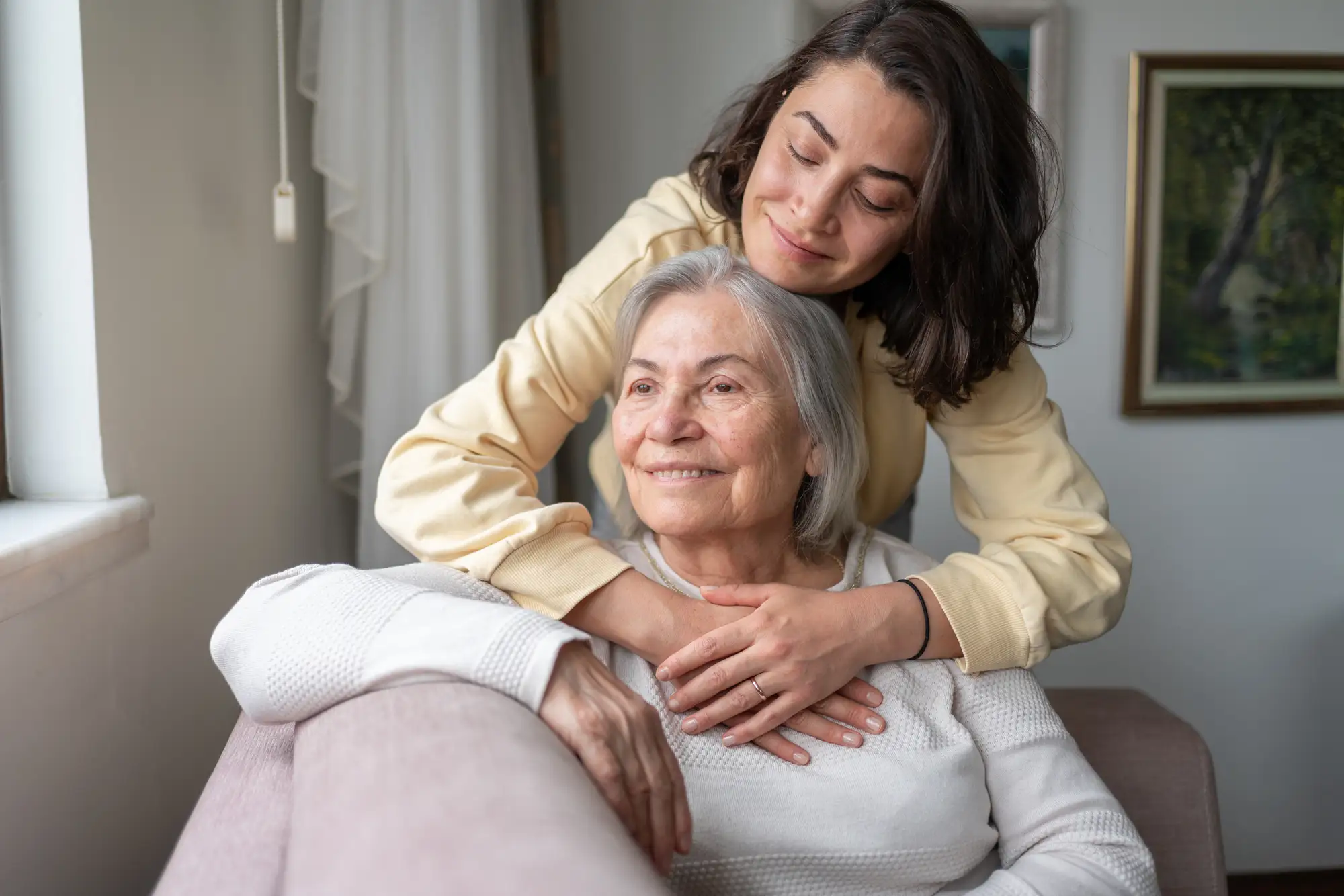An adult daughter hugging her senior mother in her home at the Village at Proprietors Green in Marshfield, MA.
