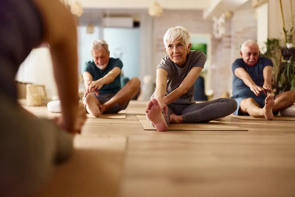 What Happens When Wellness for Seniors Becomes Part of Everyday Life 1 Seniors at Village at Proprietors Green practice seated leg stretches on exercise mats during a indoor yoga or fitness class, prioritizing flexibility and wellness for seniors.