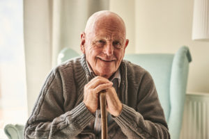 Senior man sitting with his hands folded over a walking stick